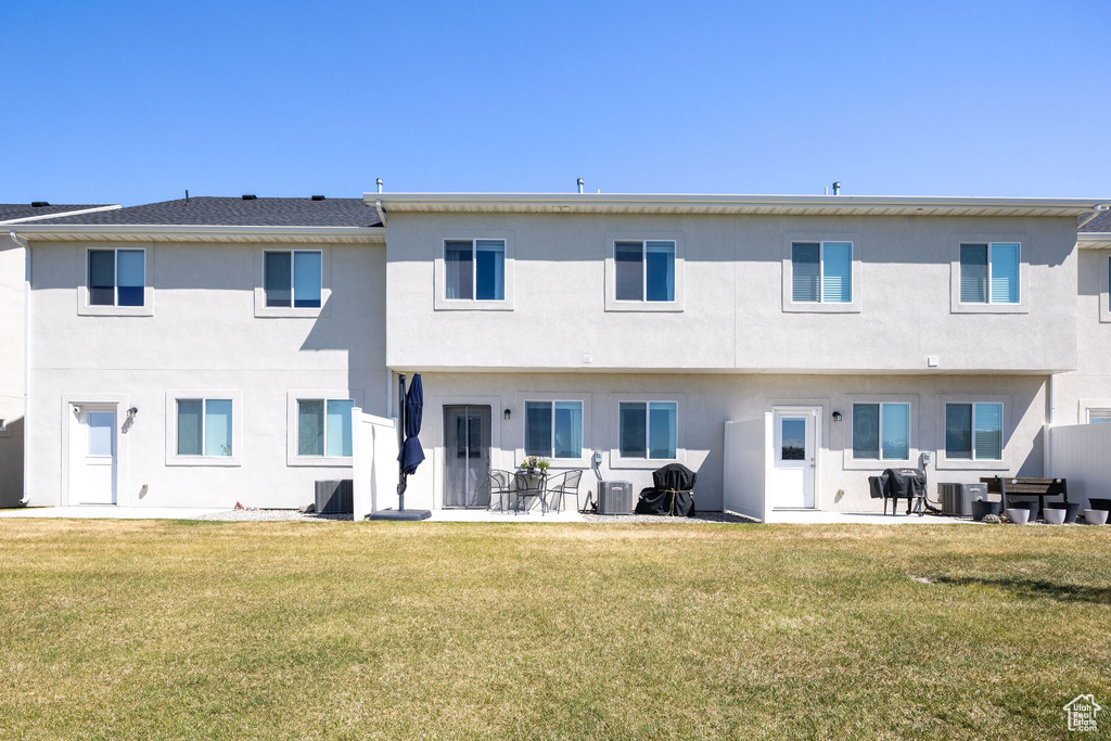 Rear view of property with a lawn, central AC unit, and stucco siding