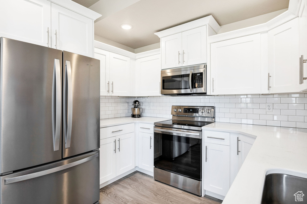 Kitchen featuring appliances with stainless steel finishes, light countertops, white cabinetry, light wood finished floors, and recessed lighting