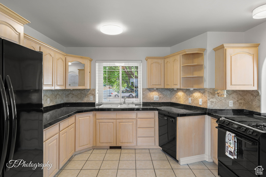 Kitchen featuring black appliances, light brown cabinets, a sink, light tile patterned flooring, and backsplash