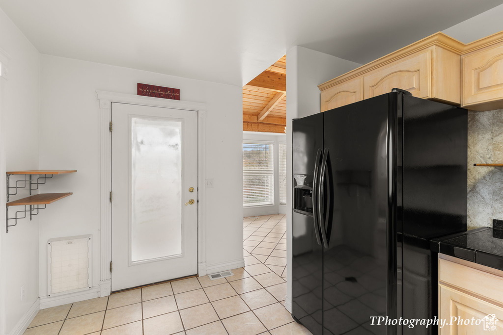 Kitchen with black refrigerator with ice dispenser, light brown cabinets, beamed ceiling, light tile patterned floors, and baseboards