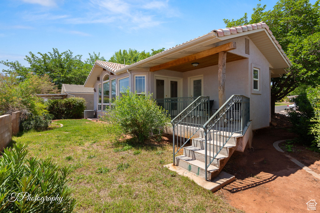 Back of property with stucco siding, a yard, a tile roof, and cooling unit