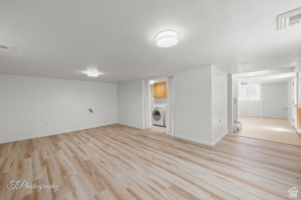 Finished below grade area featuring washer / dryer, light wood-style floors, baseboards, and a textured ceiling
