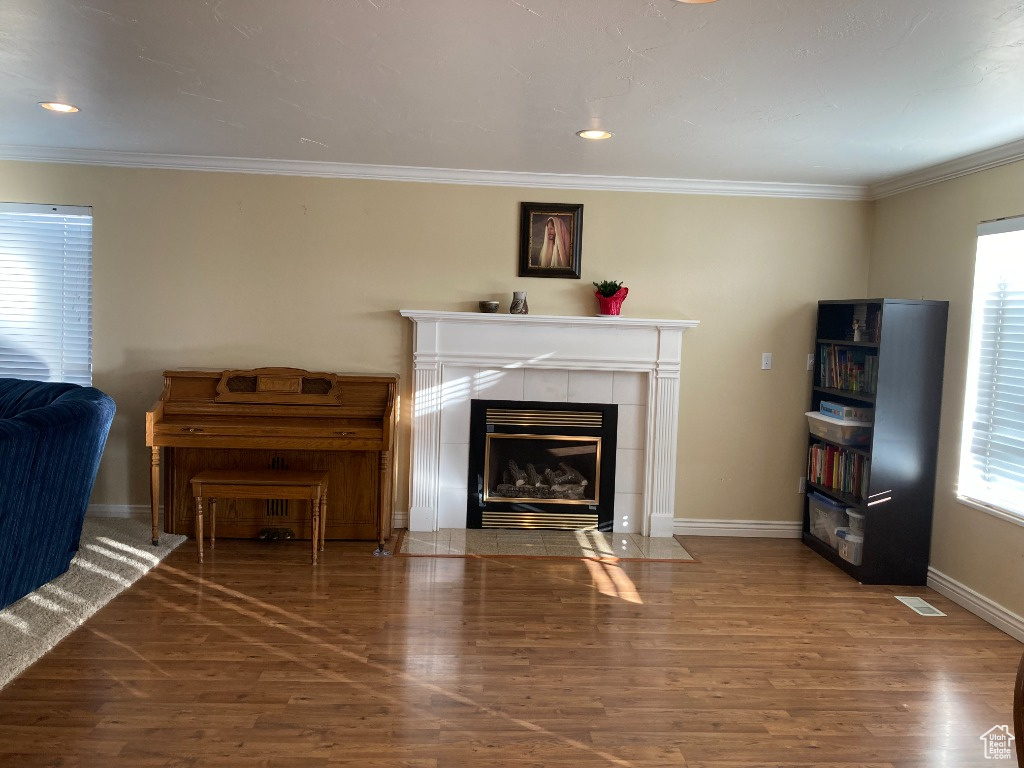 Living room with healthy amount of natural light, a tiled fireplace, wood finished floors, baseboards, and crown molding
