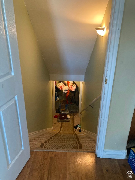 Stairway with wood finished floors, lofted ceiling, and baseboards