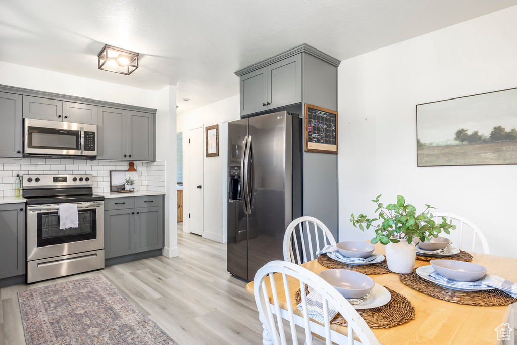 Kitchen featuring stainless steel appliances, gray cabinets, backsplash, light countertops, and light wood finished floors