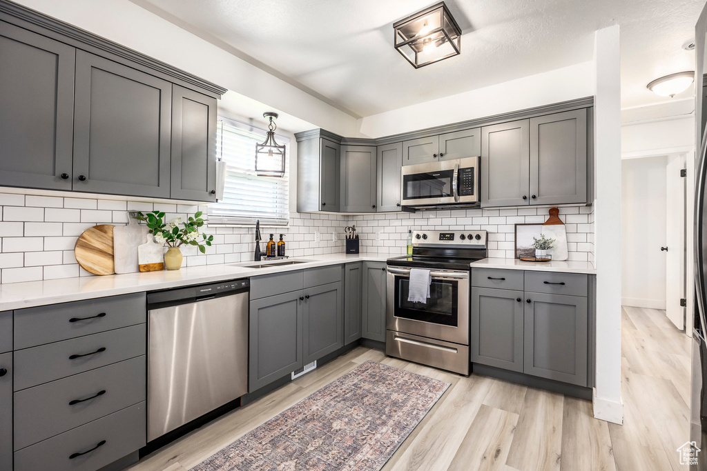 Kitchen with stainless steel appliances, a sink, gray cabinets, light wood-style floors, and light countertops