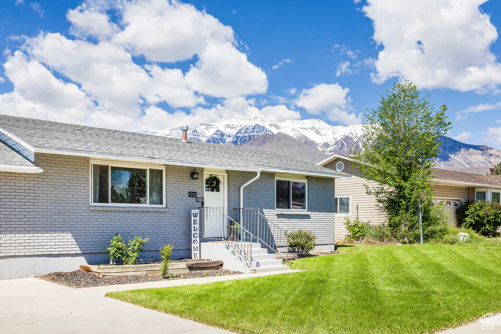 Ranch-style home with a mountain view, a front yard, brick siding, and a shingled roof