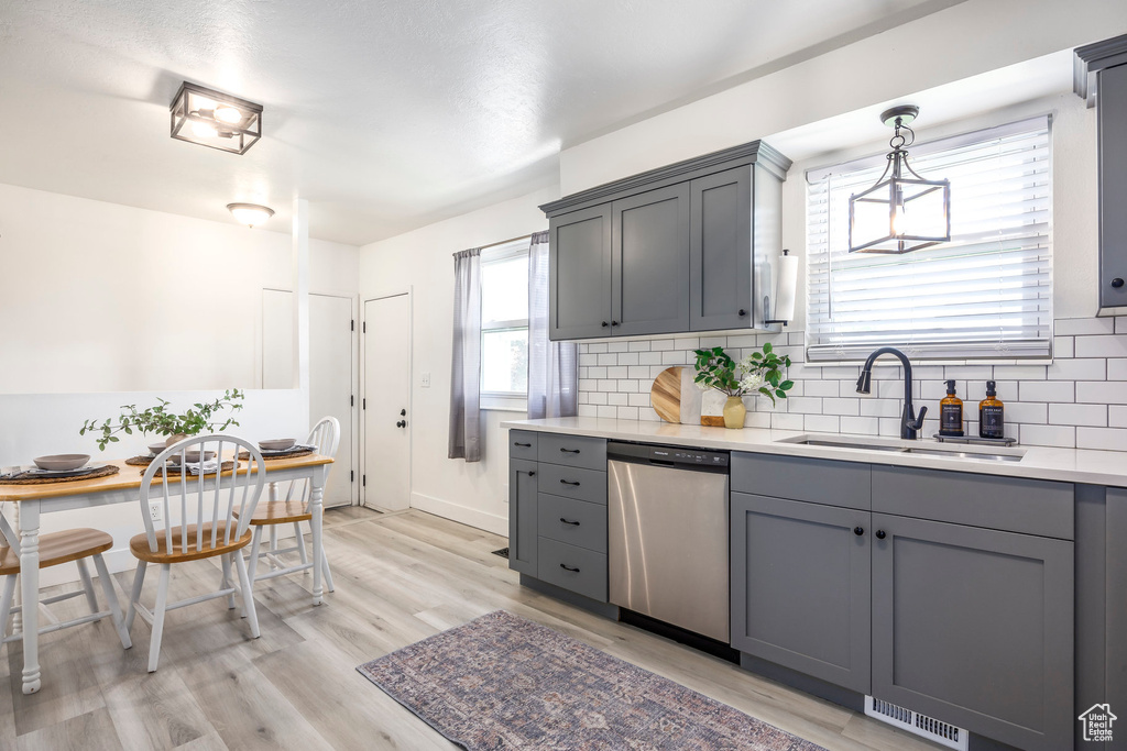 Kitchen with stainless steel dishwasher, a sink, gray cabinets, decorative backsplash, and light countertops