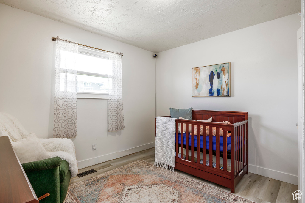 Bedroom featuring baseboards, wood finished floors, a textured ceiling, and a crib
