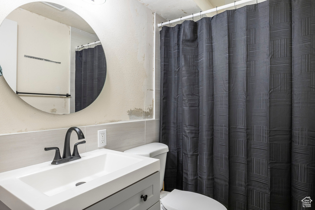 Full bathroom with tile walls, toilet, vanity, and wainscoting