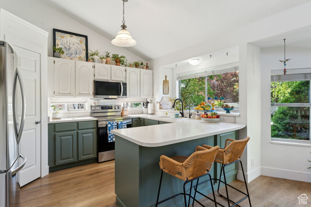 Kitchen with appliances with stainless steel finishes, a peninsula, a sink, lofted ceiling, and light wood-type flooring