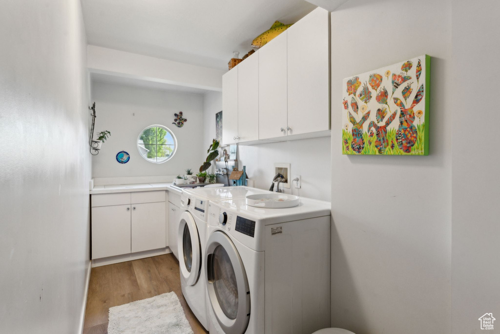 Laundry area featuring separate washer and dryer, light wood-style floors, and cabinet space