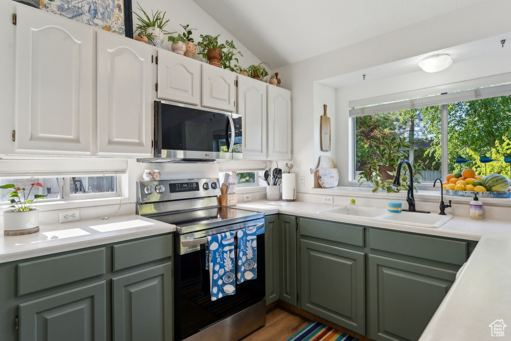 Kitchen featuring stainless steel appliances, a sink, green cabinets, light countertops, and vaulted ceiling