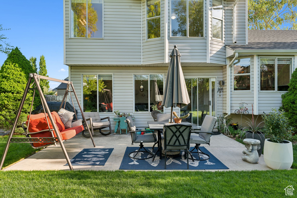Rear view of house featuring a patio, a lawn, roof with shingles, and a chimney