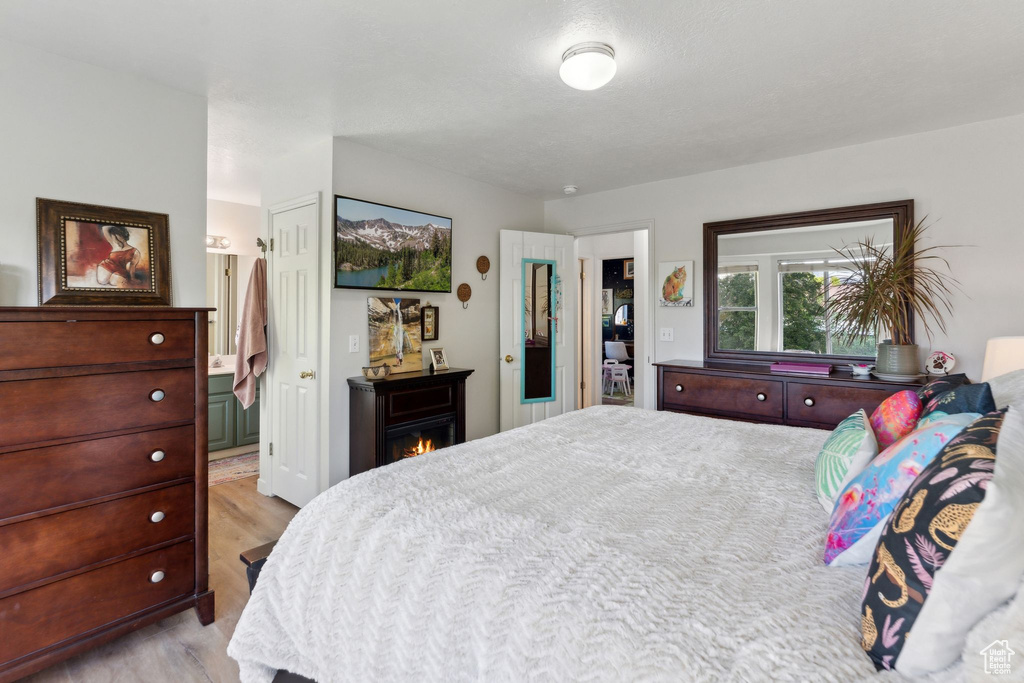 Bedroom with light wood-style flooring, a lit fireplace, and ensuite bath