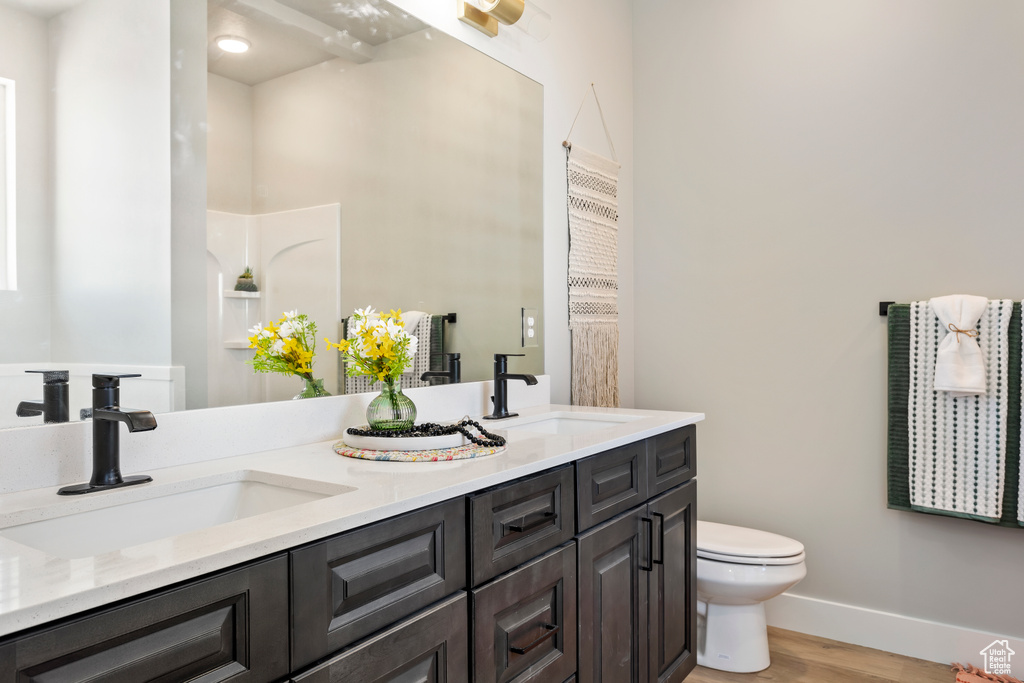 Bathroom featuring wood finished floors, toilet, double vanity, and baseboards