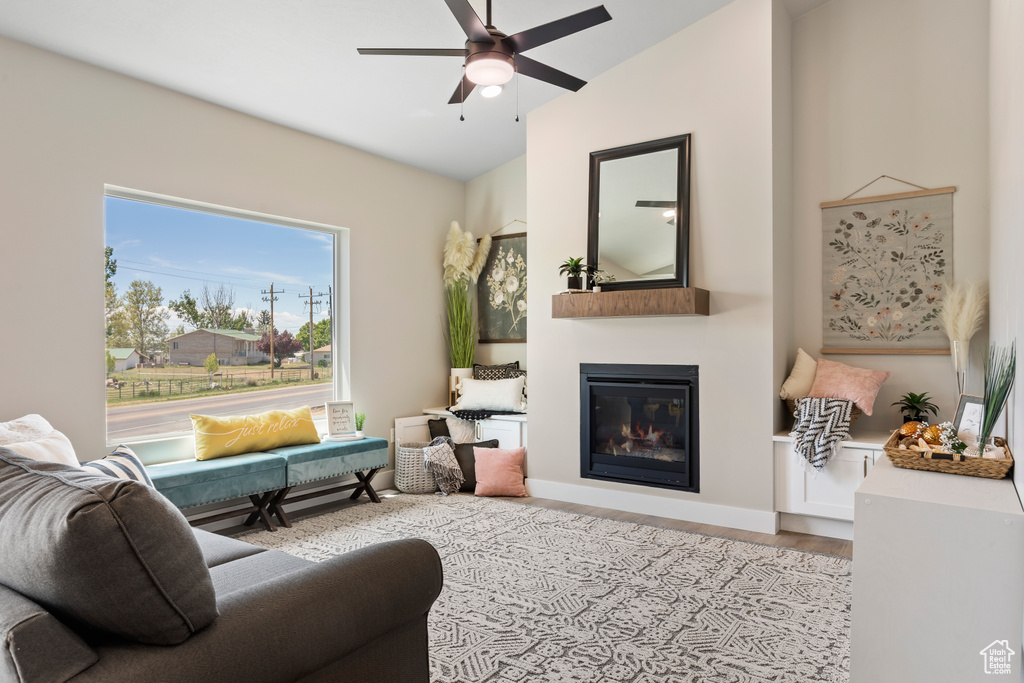 Living room with a glass covered fireplace, a ceiling fan, wood finished floors, and vaulted ceiling