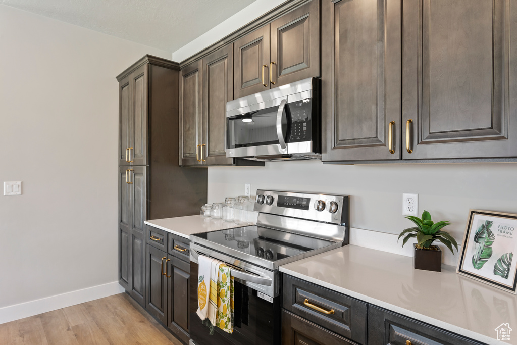 Kitchen featuring appliances with stainless steel finishes, light countertops, baseboards, light wood finished floors, and dark brown cabinetry