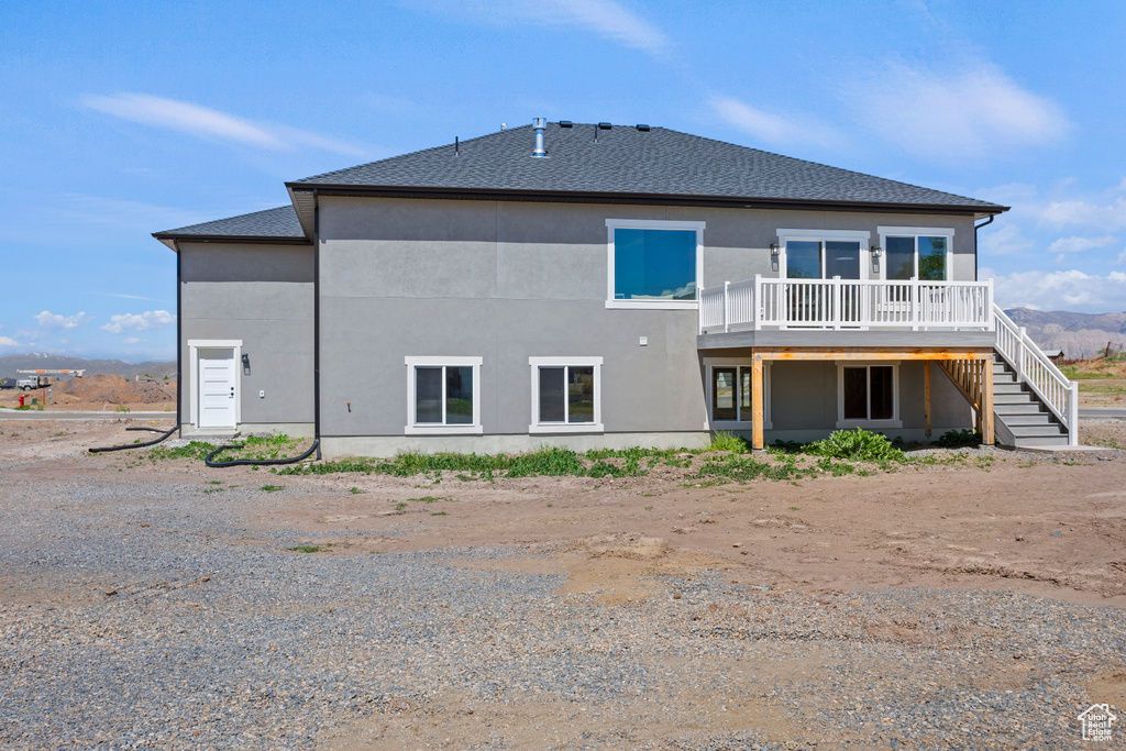Rear view of house with a deck, stairway, stucco siding, and roof with shingles