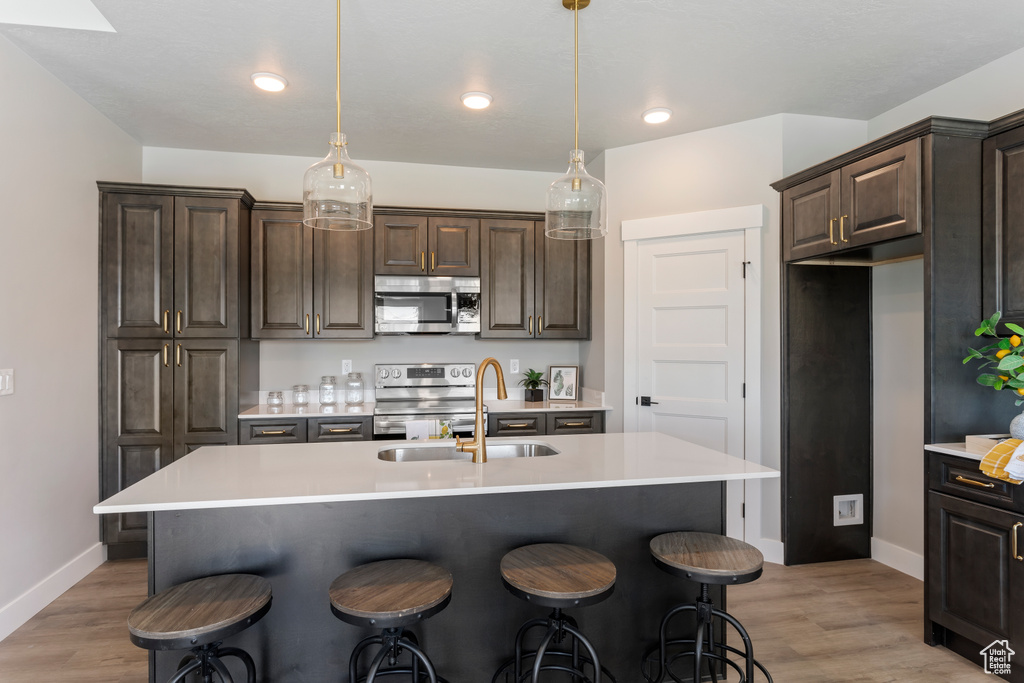 Kitchen with stainless steel appliances, a sink, light countertops, dark brown cabinets, and baseboards
