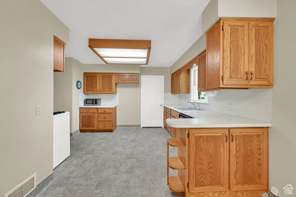 Kitchen featuring stainless steel microwave, a sink, light countertops, a peninsula, and brown cabinets