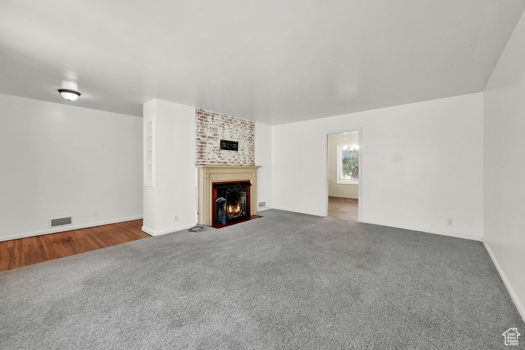 Unfurnished living room with carpet flooring, a fireplace with flush hearth, and baseboards
