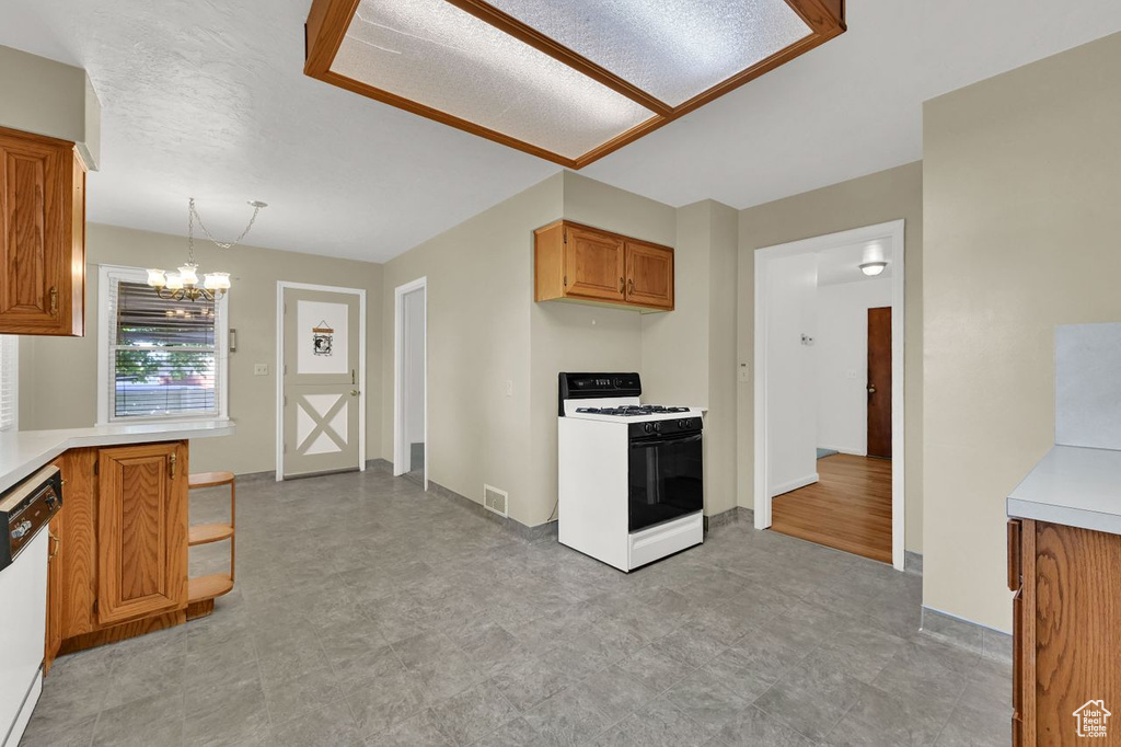 Kitchen with white appliances, light countertops, a chandelier, brown cabinets, and decorative light fixtures