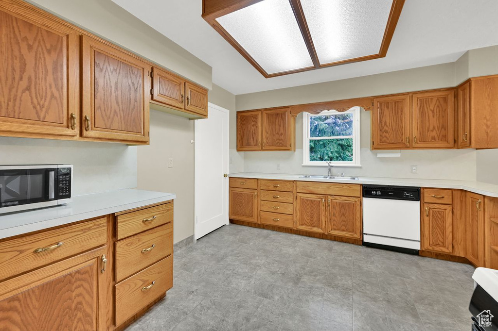 Kitchen featuring dishwasher, a sink, light countertops, and brown cabinetry