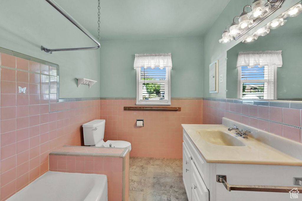 Bathroom with tile walls, a bath, wainscoting, vanity, and toilet