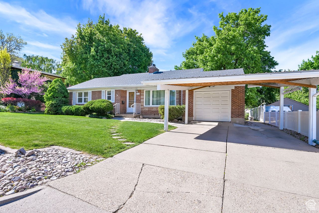 Ranch-style house featuring a garage, driveway, brick siding, a chimney, and a carport