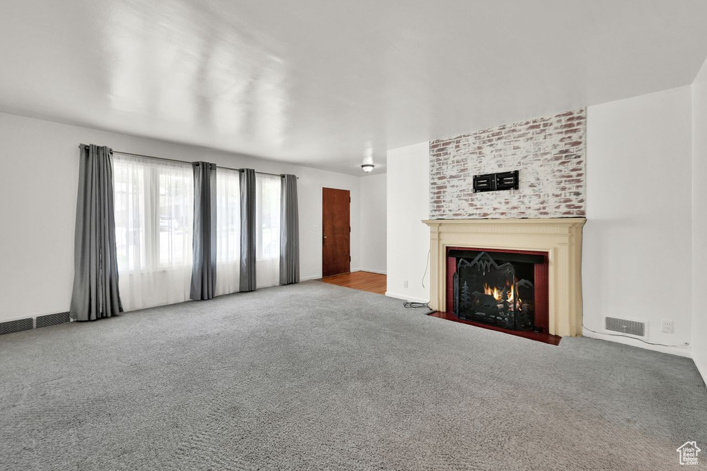 Unfurnished living room with carpet floors, a fireplace with flush hearth, and baseboards