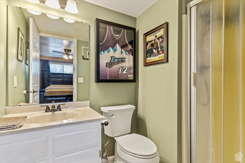 Ensuite bathroom featuring toilet, vanity, ceiling fan, and an enclosed shower
