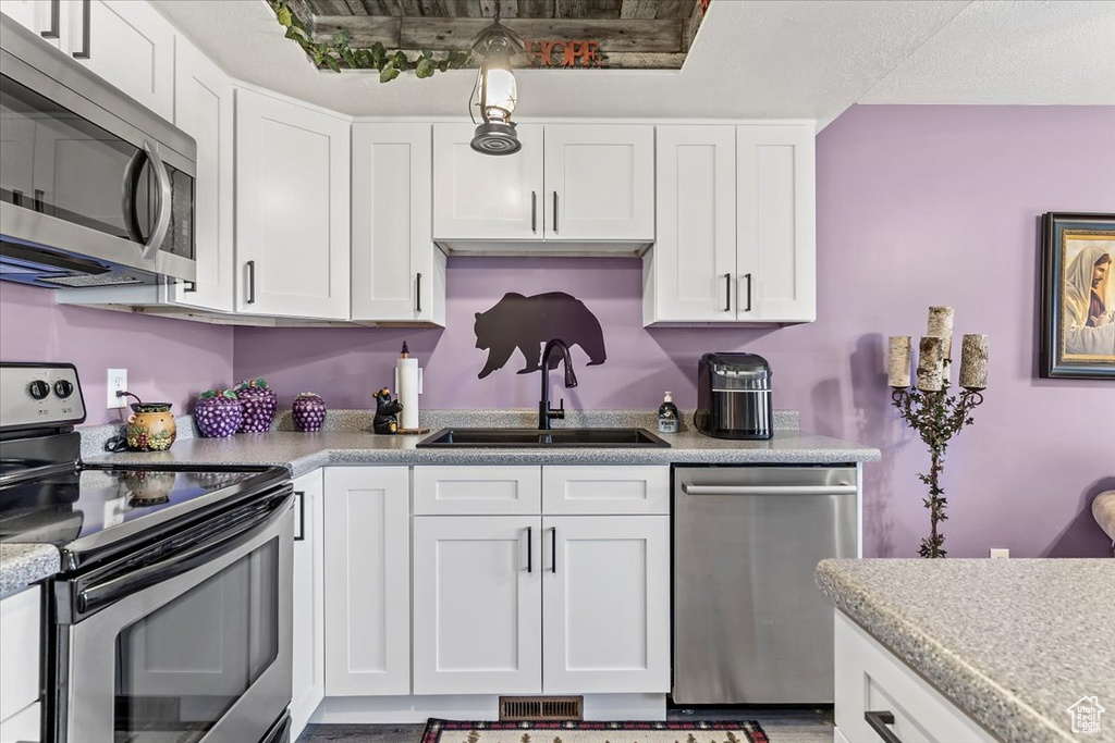 Kitchen with appliances with stainless steel finishes, a sink, white cabinetry, and light countertops