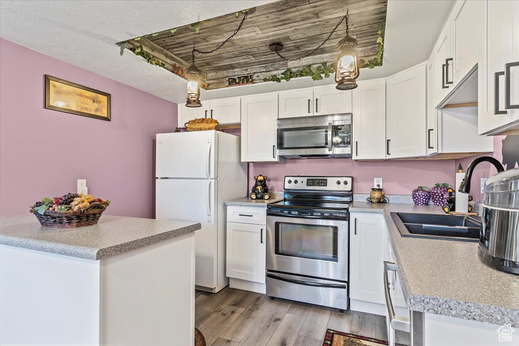 Kitchen with stainless steel appliances, a sink, light wood-type flooring, white cabinets, and light countertops