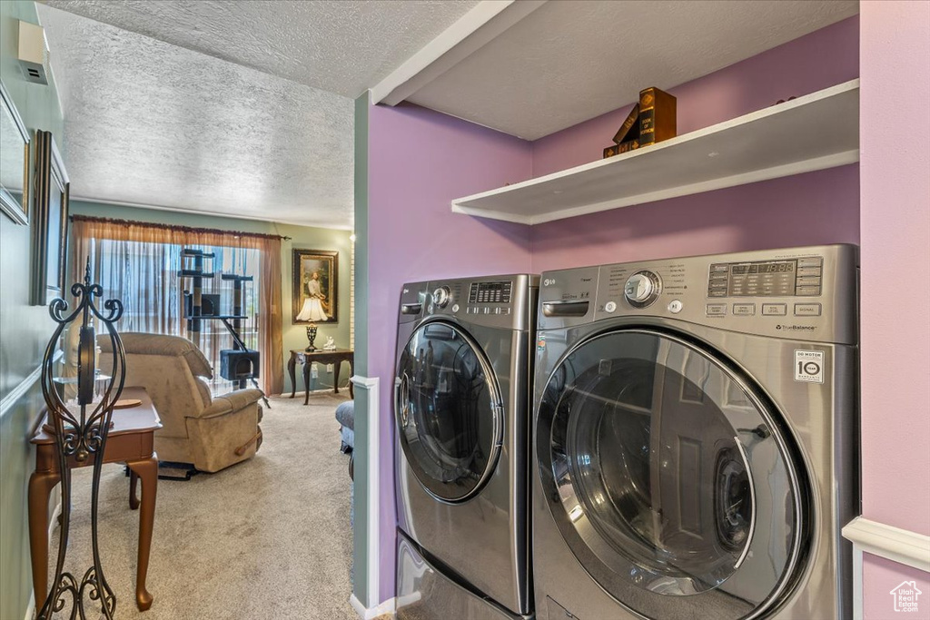 Laundry room featuring washing machine and clothes dryer, carpet flooring, and a textured ceiling