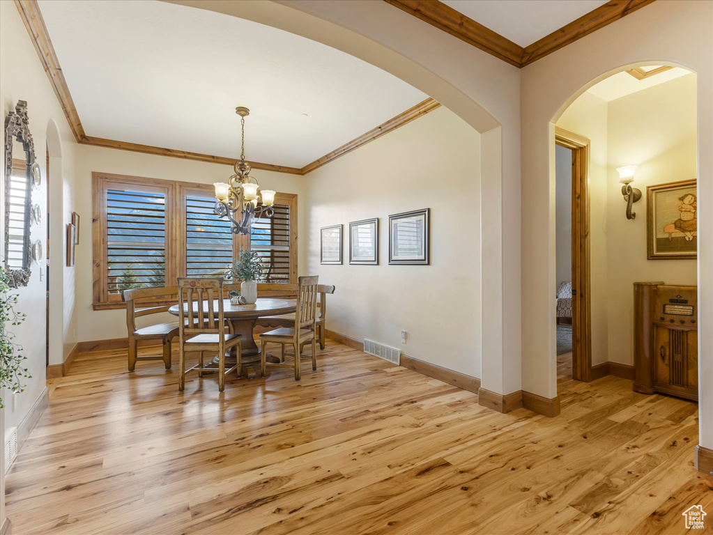 Dining room with light wood-style flooring, arched walkways, a chandelier, ornamental molding, and baseboards