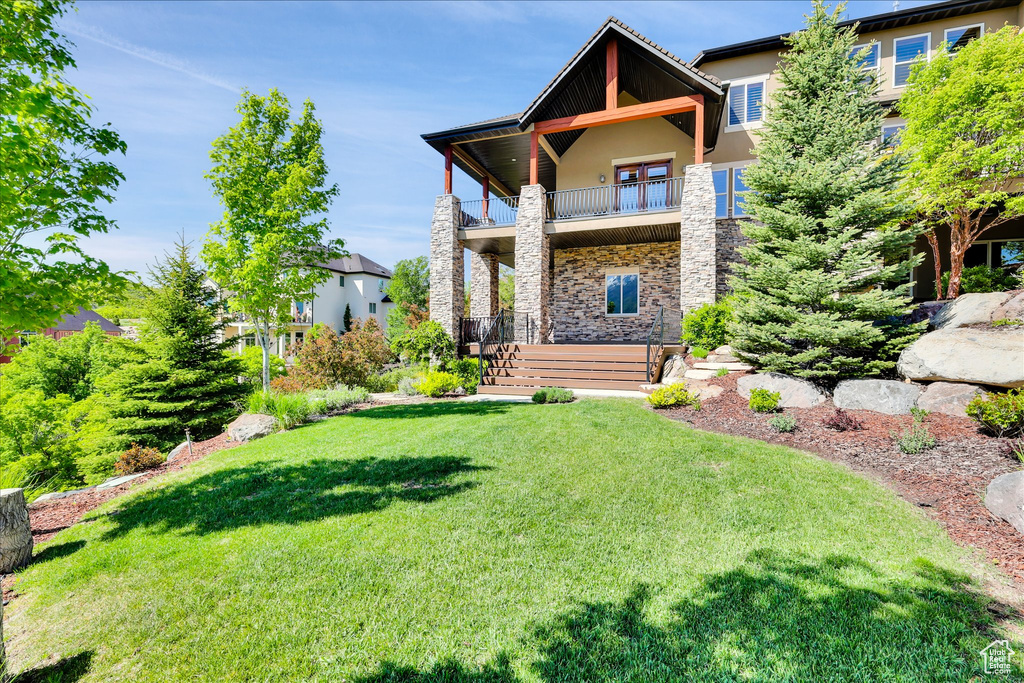 Rear view of house with stone siding, a balcony, a yard, and stucco siding