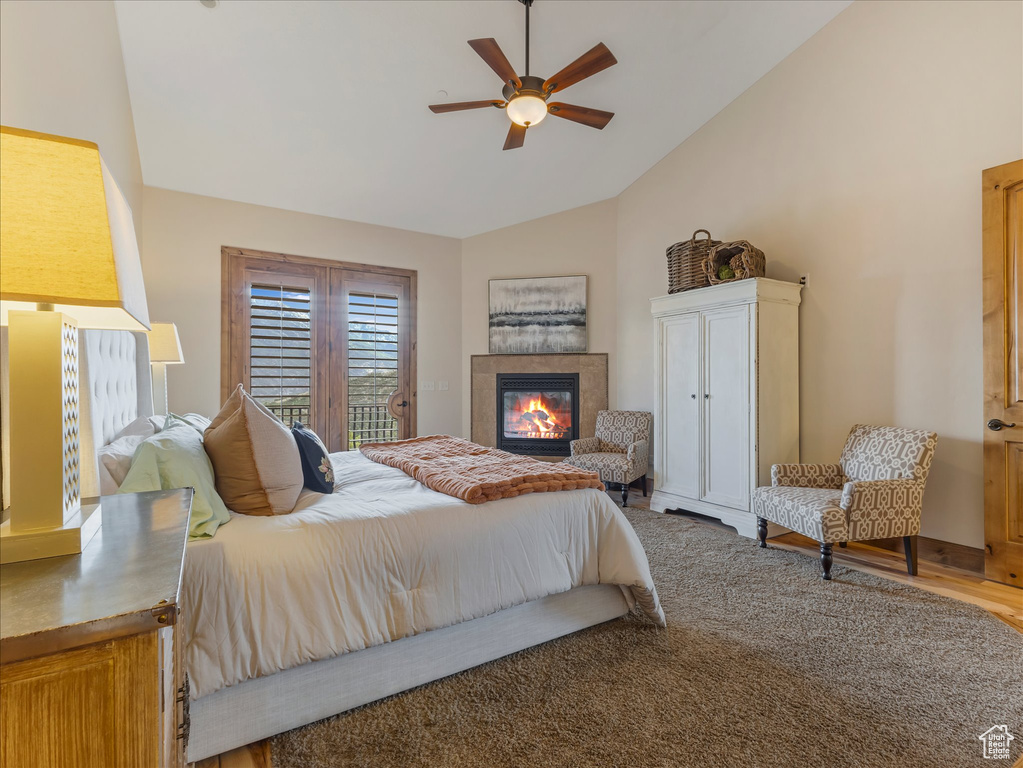 Bedroom with lofted ceiling, a tile fireplace, ceiling fan, access to exterior, and wood finished floors