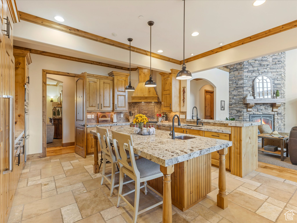 Kitchen featuring stone tile flooring, a breakfast bar, premium range hood, backsplash, and an island with sink