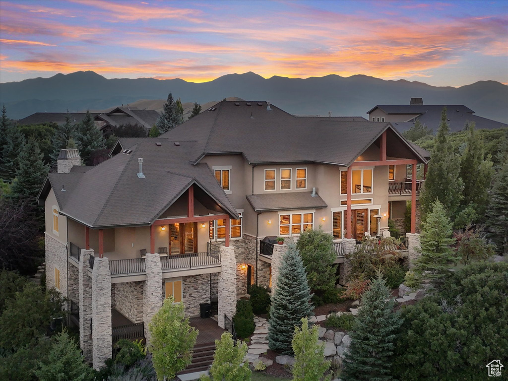 Back of house at dusk featuring a balcony, stone siding, stucco siding, and a mountain view