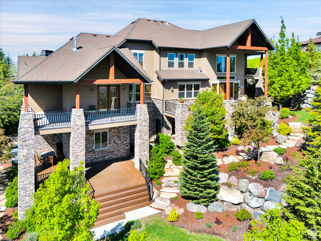 Rear view of property featuring a balcony, stucco siding, stone siding, and stairs