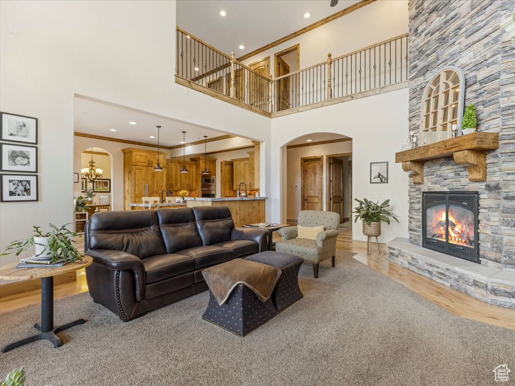 Living area with a stone fireplace, arched walkways, a high ceiling, light wood-style floors, and ornamental molding
