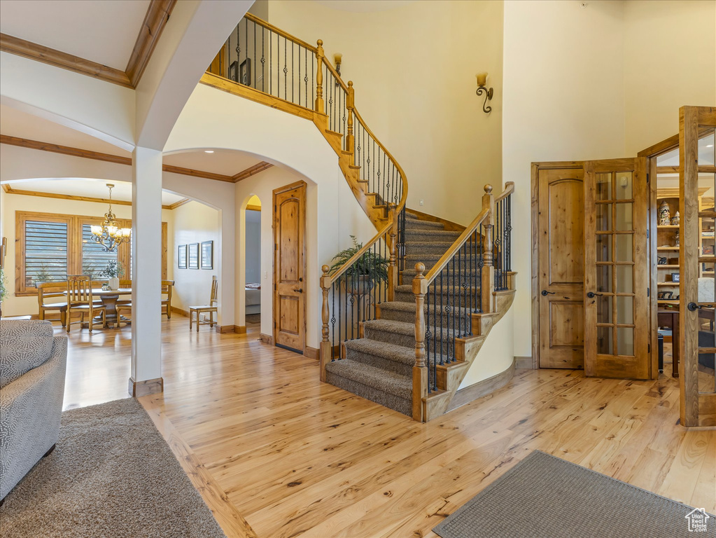 Stairs featuring crown molding, arched walkways, hardwood / wood-style floors, a chandelier, and a high ceiling