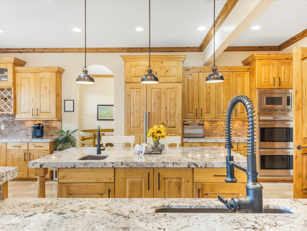 Kitchen with ornamental molding, a sink, decorative backsplash, stainless steel appliances, and light stone countertops