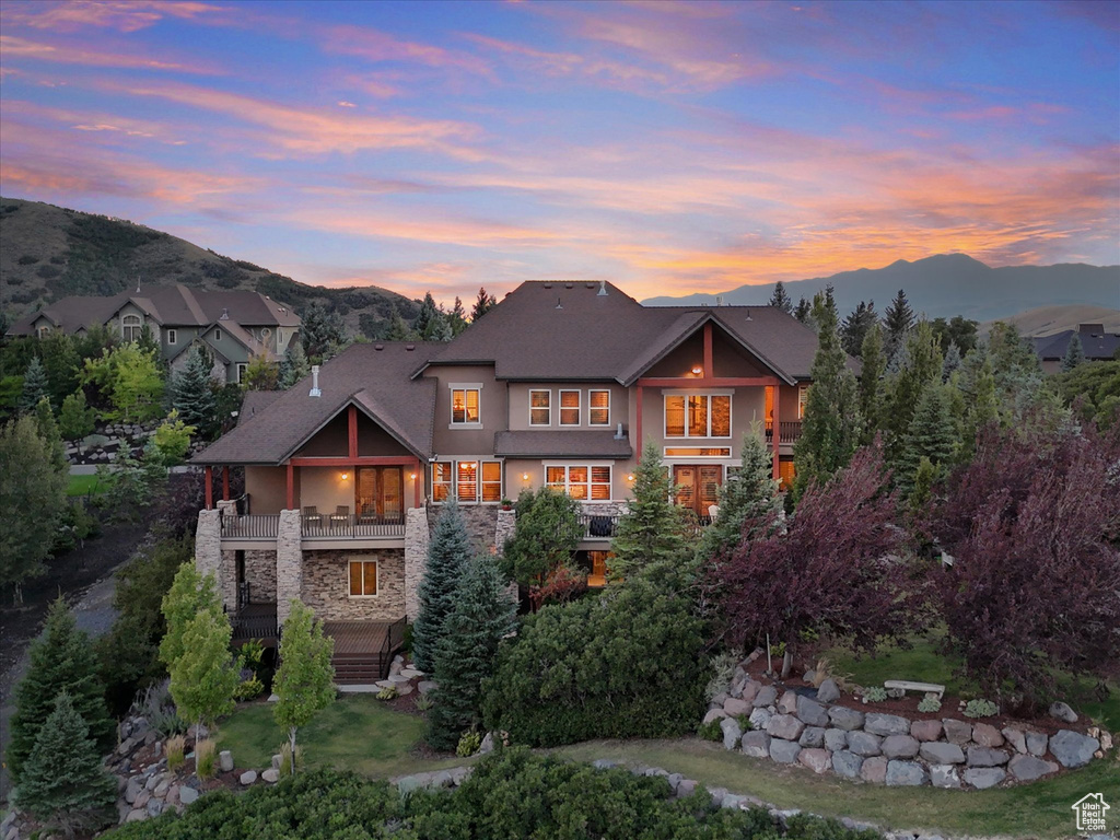 View of front of house with stucco siding, stone siding, a balcony, and a mountain view