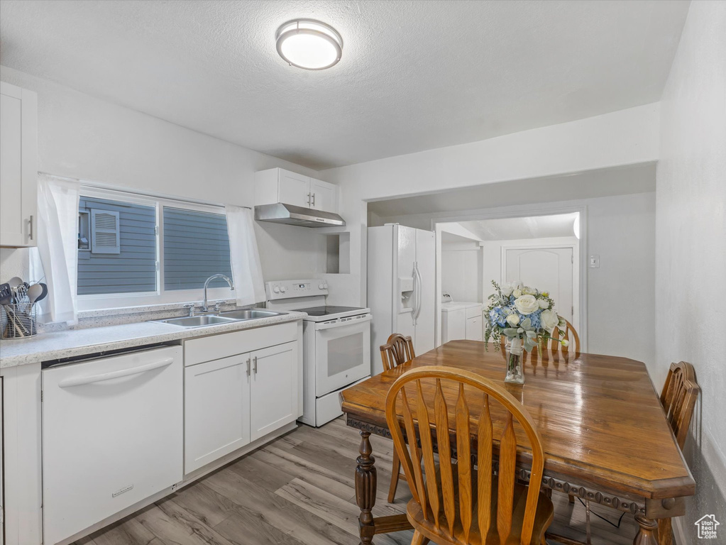 Kitchen featuring white appliances, a sink, washing machine and clothes dryer, light countertops, and white cabinetry