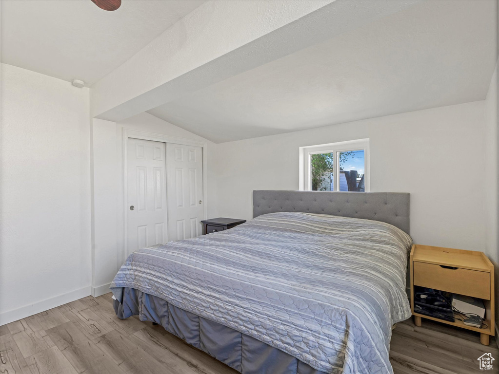 Bedroom with wood finished floors, lofted ceiling, a closet, and baseboards