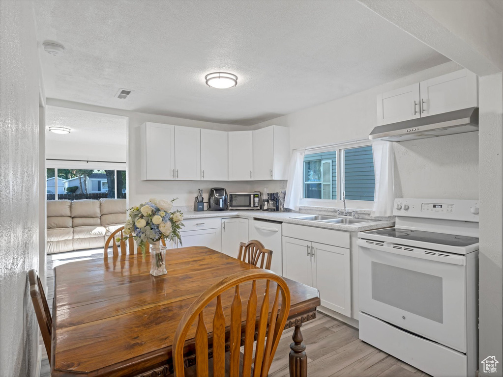 Kitchen featuring white appliances, a sink, under cabinet range hood, light countertops, and white cabinets
