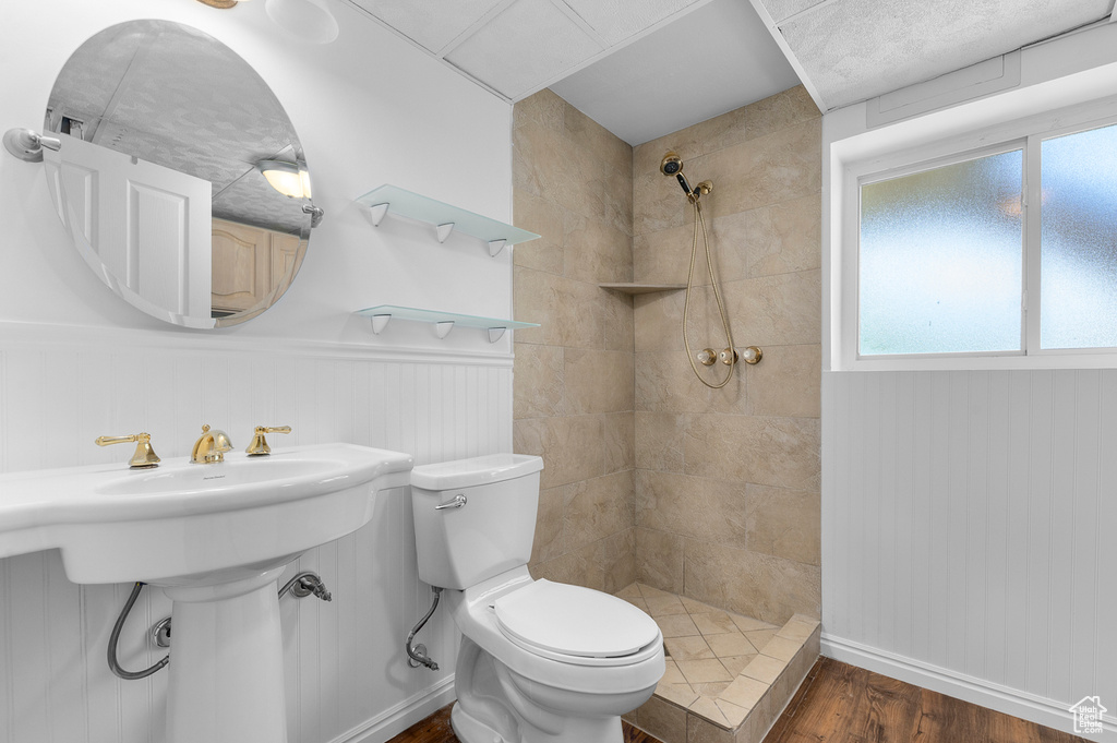 Full bath with a tile shower, toilet, wood finished floors, a sink, and baseboards