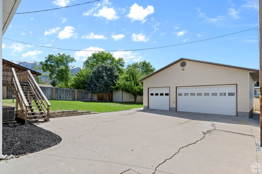 View of side of home with an outdoor structure, stairs, central air condition unit, a detached garage, and a mountain view